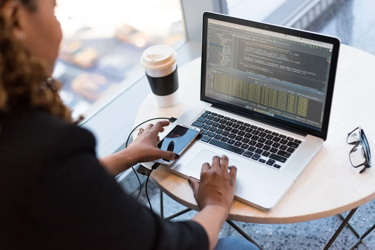 Developer working on a laptop at a desk with coffee and a phone